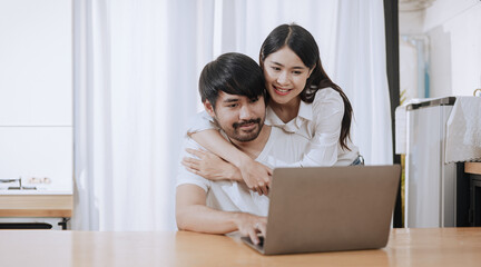 Happy love Asian young man and woman using laptop together in the kitchen relaxing at home.