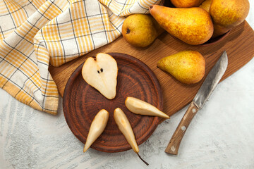 Clay plate with slices and half of pear, wicker basket and yellow kitchen towel on wooden cutting board..