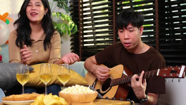 Man playing guitar at home with his friends at a party.group of young asian female and thai male happy smiling and sing a song with friends in birthday party at home