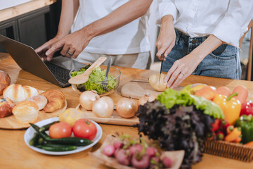 Happy love Asian young man and woman cooking food together in the kitchen relaxing at home.