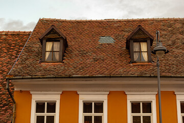 Fototapeta na wymiar Old house with red clay tiles and wooden windows in Transylvania. The roof was repaired with new tiles. Emergency roof repair. Historic architecture against a cloudy sky
