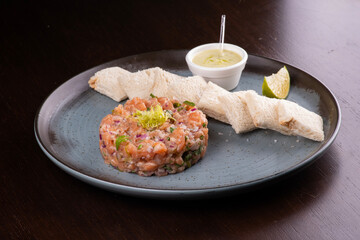 Raw salmon tartare with toast sauce and lemon on rustic ceramic plate