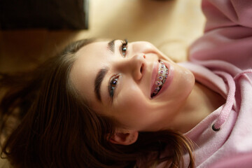 Close up portrait of beautiful, cheerful woman with braces lying on floor and smiling looking up....