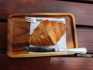 Croissants are served on a wooden plate with a knife and fork.
