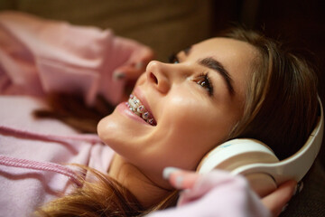 Close up portrait of beautiful young lady lying on floor and dreamy looking up while listening...