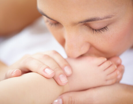 Mom, baby and kiss feet of child for love, care and relax in nursery room at home. Face, mother and closeup of foot of young kid for newborn development, healthy childhood growth or affection of bond