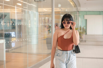 A fashionable young Asian woman with sunglasses strolls through a modern mall, looking casually chic.