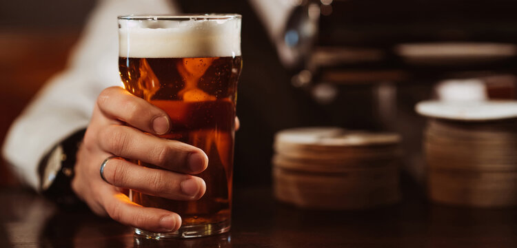 bartender's hand with a glass of light draft beer with foam in bar close-up