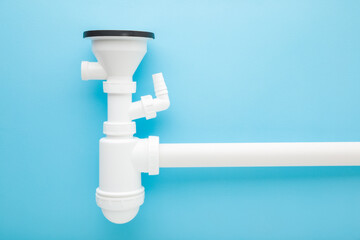Assembled white new plastic parts for sink drain siphon on light blue table background. Pastel...