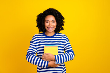 Portrait of intelligent good mood girl with afro hair wear striped sweatshirt embrace book in library isolated on yellow color background