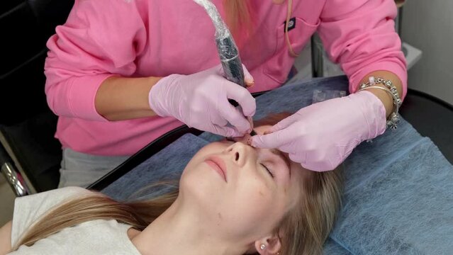 Beauty treatment. Young woman undergoing procedure of eyebrow permanent makeup in beauty salon . A beautician performs modeling of permanent eyebrows . Permanent tattooing of eyebrows.