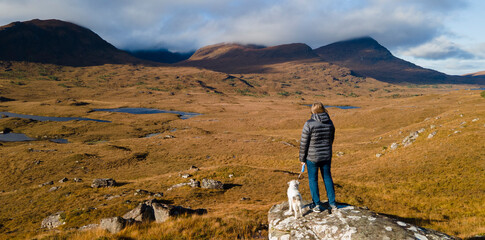 Woman and dog looking out over mountain view in Scotland