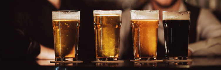 four glasses with different beers on bar counter in pub against the background of bartenders
