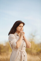 portrait of young woman praying on nature, girl thanks God with her hands folded under chin,...
