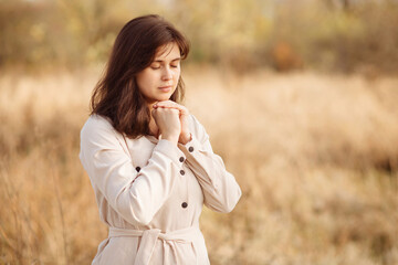 portrait of young woman praying on nature, girl thanks God with her hands folded under chin, concept of religion