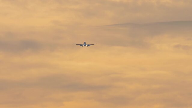 Jet plane approaching to land, descending at the sunset sky. Footage of an airplane flying, front view. Tourism and travel concept. Aircraft arriving