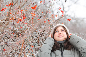 Portrait of young beautiful brunette woman in winter clothes walking on nature, girl standing near viburnum and looking up