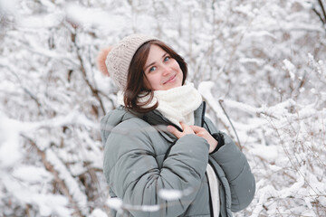 happy young woman in knitted hat and warm scarf among trees covered with snow, girl walking on winter forest enjoying beautiful nature