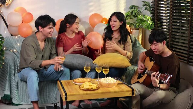 Man playing guitar at home with his friends at a party.group of young asian female and thai male happy smiling and sing a song with friends in birthday party at home