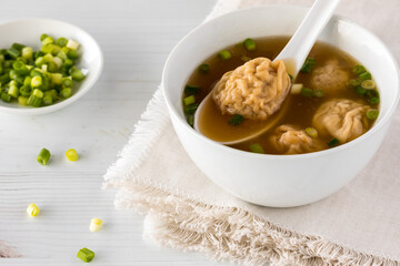 A bowl of wonton soup garnished with green onion.