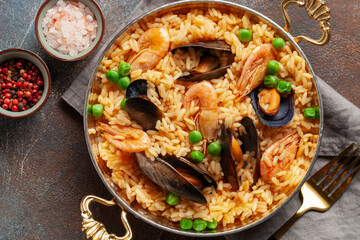 Traditional spanish seafood paella with rice, mussels, shrimps in a pan on wooden background. Top...