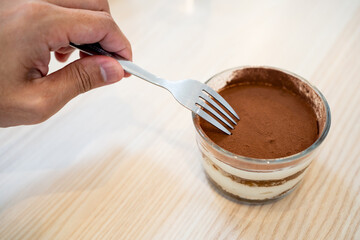 Hand pointing fork into Tiramisu cake surface.