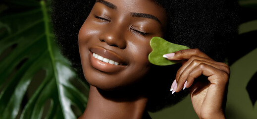 Gua Sha jade skin treatment. African American model making face massage  with a stone tool against...