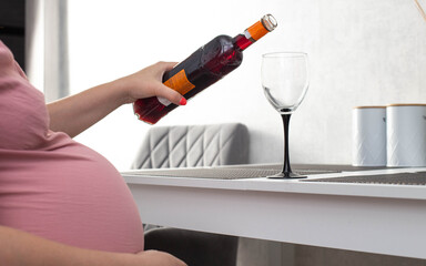 A pregnant girl pours wine from a bottle into a glass. The concept of drinking alcohol during pregnancy. Harm and cognitive impairment in a child. Alcoholism, copy space for text - obrazy, fototapety, plakaty