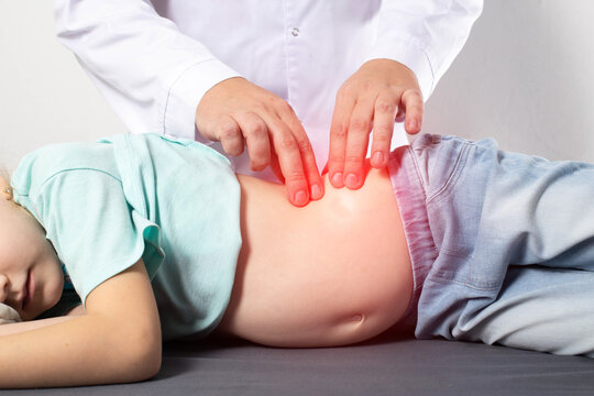 A doctor surgeon examines and diagnoses the abdomen of a seven-year-old little girl who has abdominal pain. Concept of appendicitis in children, nausea and discomfort.