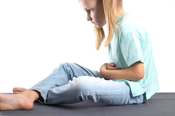 A seven-year-old blonde caucasian girl sits and holds her stomach. The concept of abdominal pain in...