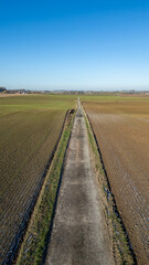 Fototapeta na wymiar This image presents a vertical, linear perspective of a country road cutting through the winter fields. On either side, the contrast between the harvested field and the one awaiting cultivation is