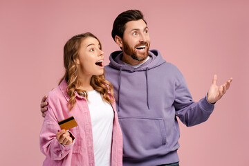 Smiling couple holding credit card and feeling happy, shopping online isolated on pink background....
