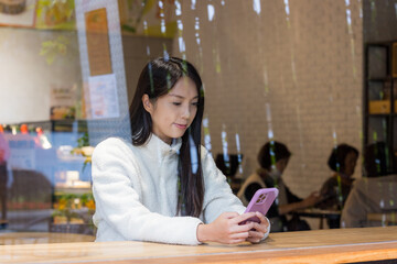 Woman look at the mobile phone and sit inside the coffee shop