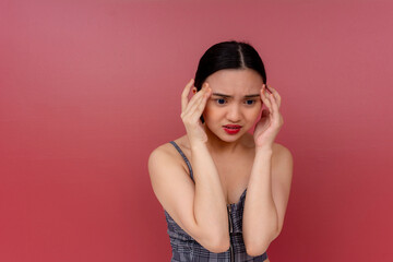 A worried young asian woman unsure of what to do. Massing her temples, deeply concerned about something. Isolated on a red background.