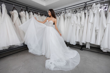 Beautiful young bride is trying on a white wedding dress against the background of a large number...