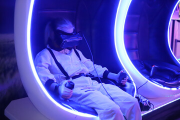 Girl in ultraviolet light in chair wearing virtual reality glasses playing games in amusement park computer games