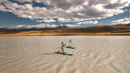 Two young girls tourists walks on stand up paddle boards sup at white mountain lake