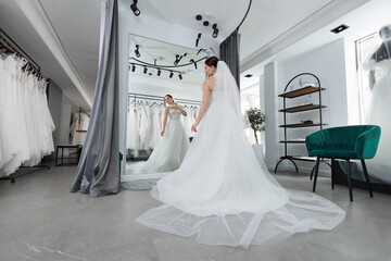 Gorgeous slender bride tries on a wedding dress in a beauty salon in front of a mirror.
