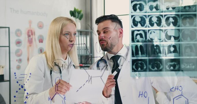 Man and Woman doctors which standing near glass wall with patient's x-ray image and talking to each other about diagnosis