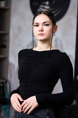 Waist portrait of stylist dark haired woman with plaits in black jumper standing in barbershop.