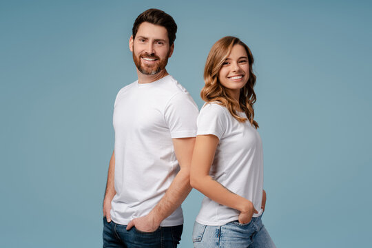 Portrait of attractive smiling couple posing isolated on blue background. Happy bearded man and beautiful woman wearing stylish white t shirt looking at camera in studio