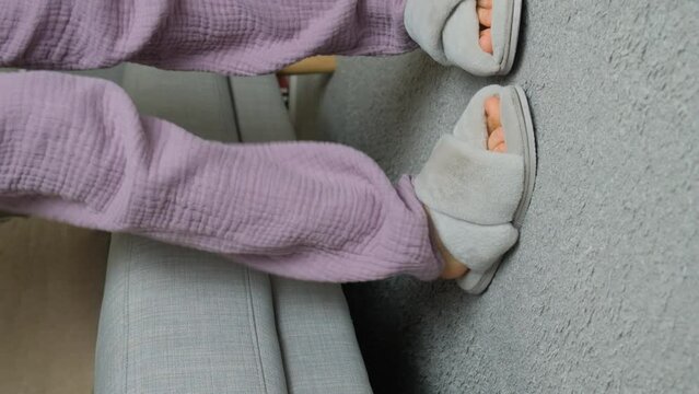 Woman in fluffy slippers at home sits on the sofa and takes off her shoes. Vertical slow motion shooting