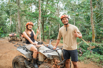 the asian man standing with thumb up in front of the atv rided by the asian woman © Odua Images