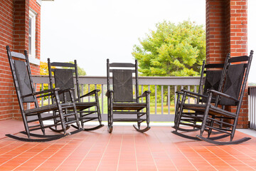  Five high back wicker rockers on red tiled porch with red brick columns, tree in field beyond