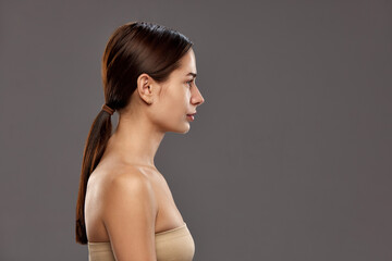 Profile view of beautiful young woman with ponytail, wearing strapless top against studio...