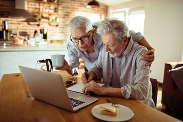 Senior couple working on laptop and discussing over coffee at home
