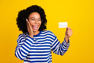 Portrait of ecstatic satisfied girl with afro hairstyle in eyewear look at debit card arm on cheek...