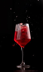 splash shot glass of iced cocktail with red campari fruits isolated on dark background