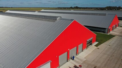 A complex of long, huge metal sheds with sloping roofs for housing and milking herds of cows. A huge farm for breeding and keeping cattle. Red facade of a metal hangar. © Aerial Drone Master