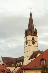 Fototapeta na wymiar The Cathedral of Saint Mary in Sibiu, Romania. Clock Tower with a pattern tile roof against the cloudy sky. A church tower of Saint Mary Evangelical Cathedral in the old city center, in Transylvania